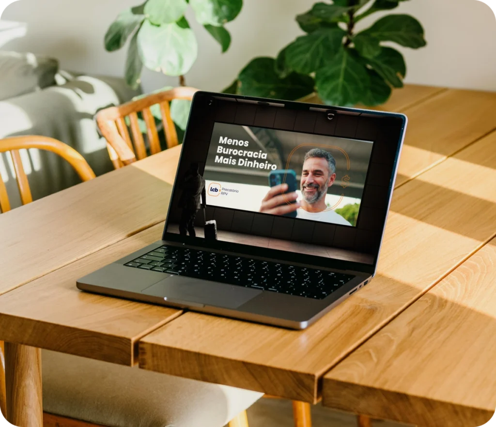 Laptop na mesa exibindo vídeo do LCbank sobre menos burocracia e mais dinheiro.